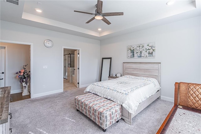 carpeted bedroom featuring a tray ceiling, ensuite bath, and ceiling fan