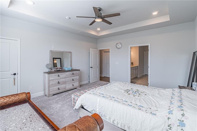 bedroom with ceiling fan, a raised ceiling, and ensuite bathroom