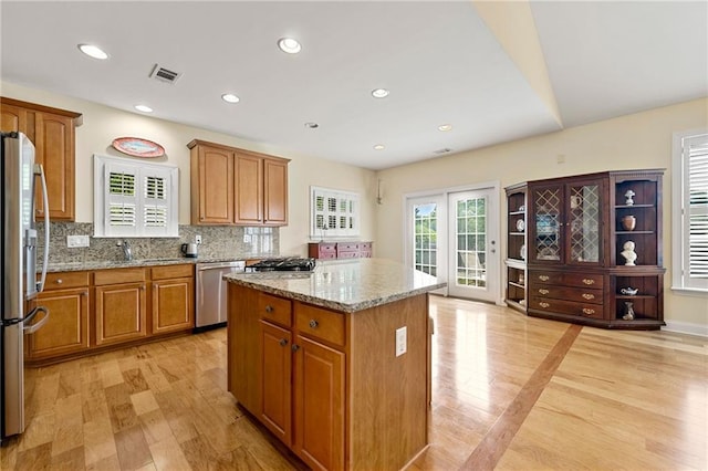 kitchen featuring stainless steel appliances, a center island, light wood-style floors, light stone counters, and recessed lighting