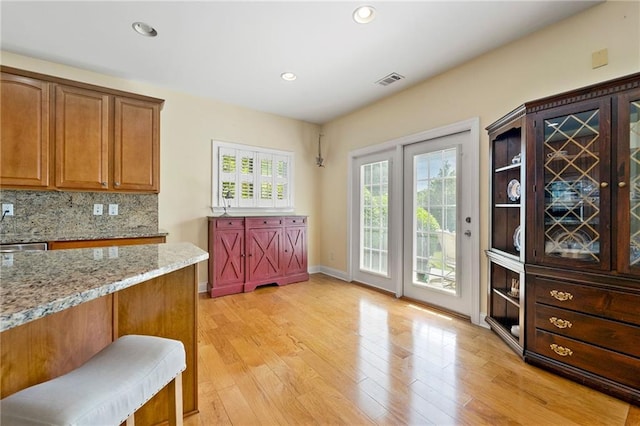 kitchen with light stone counters, brown cabinets, backsplash, light wood-type flooring, and baseboards