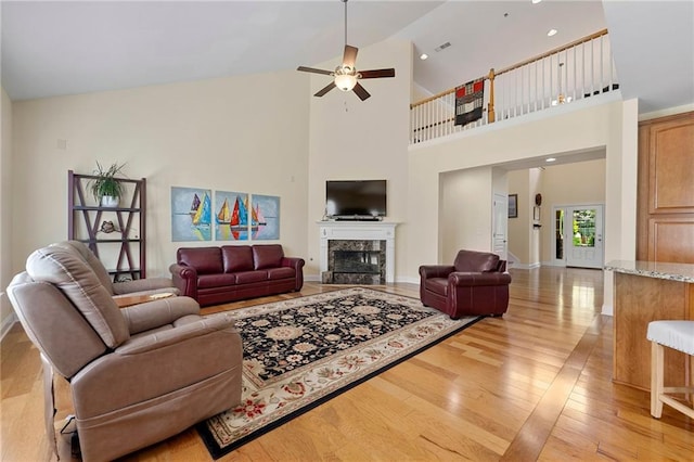 living area featuring light wood finished floors, a ceiling fan, a high end fireplace, a high ceiling, and baseboards
