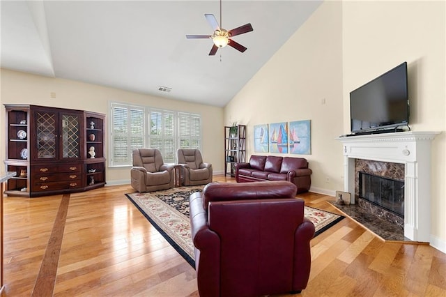 living area with ceiling fan, high vaulted ceiling, light wood-type flooring, a fireplace, and baseboards