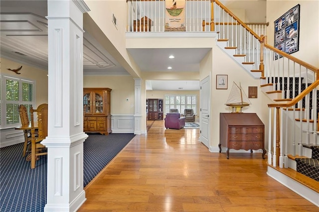 foyer entrance featuring decorative columns, plenty of natural light, stairs, ornamental molding, and a high ceiling