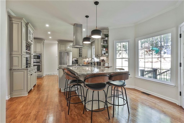 kitchen featuring decorative light fixtures, a large island with sink, light stone countertops, stainless steel appliances, and island range hood