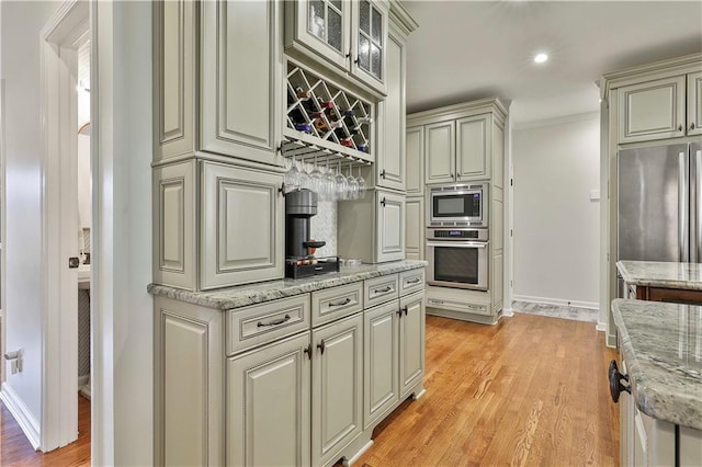 kitchen with crown molding, light wood-type flooring, light stone countertops, stainless steel appliances, and cream cabinets