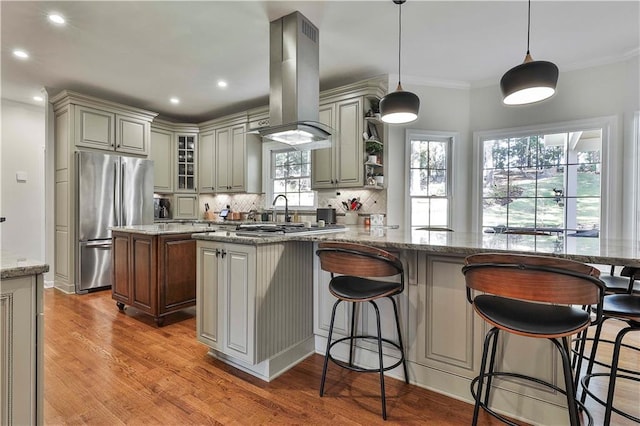 kitchen with island range hood, stainless steel fridge, decorative light fixtures, light stone counters, and a center island