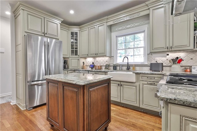 kitchen featuring light stone countertops, a center island, sink, stainless steel refrigerator, and light wood-type flooring