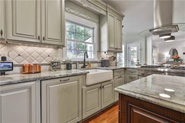 kitchen featuring island exhaust hood, plenty of natural light, light stone counters, and sink