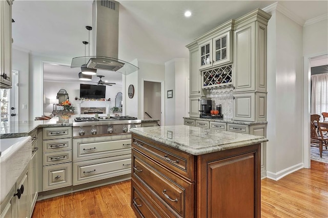 kitchen featuring stainless steel gas stovetop, island range hood, light wood-type flooring, light stone countertops, and a kitchen island