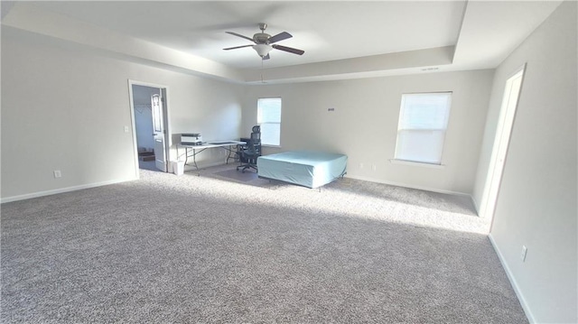 interior space with carpet floors, ceiling fan, baseboards, and a raised ceiling