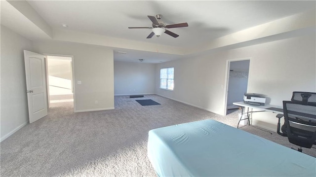 carpeted bedroom with baseboards, a tray ceiling, and a ceiling fan