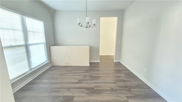 unfurnished dining area featuring plenty of natural light, baseboards, a chandelier, and wood finished floors