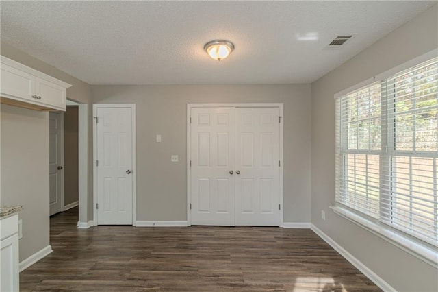 unfurnished bedroom with dark hardwood / wood-style flooring, a textured ceiling, and two closets