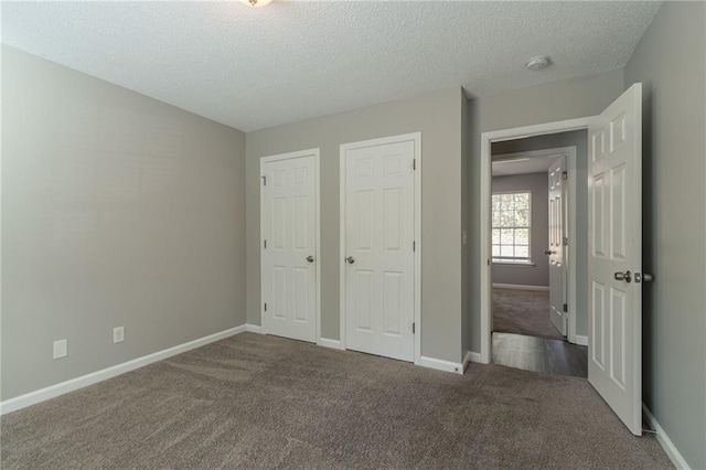 unfurnished bedroom with carpet floors, a textured ceiling, and two closets