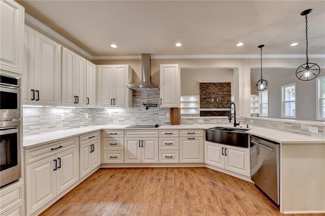 kitchen with decorative light fixtures, light countertops, appliances with stainless steel finishes, a sink, and wall chimney exhaust hood