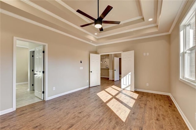 unfurnished bedroom featuring baseboards, wood finished floors, ensuite bathroom, a tray ceiling, and crown molding