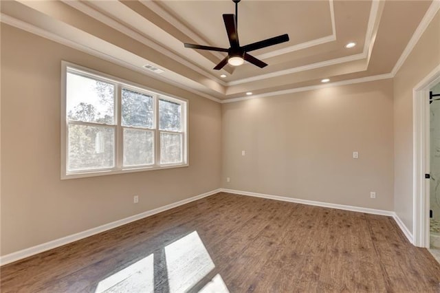 empty room with a tray ceiling, crown molding, baseboards, and wood finished floors