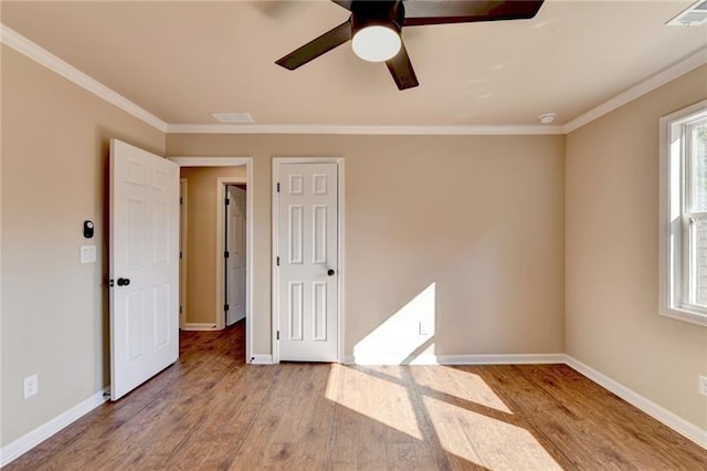 empty room featuring light wood finished floors, baseboards, visible vents, and crown molding