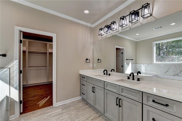 full bathroom featuring a spacious closet, double vanity, a sink, and crown molding