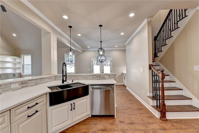 kitchen featuring light wood finished floors, decorative light fixtures, light countertops, stainless steel dishwasher, and a sink