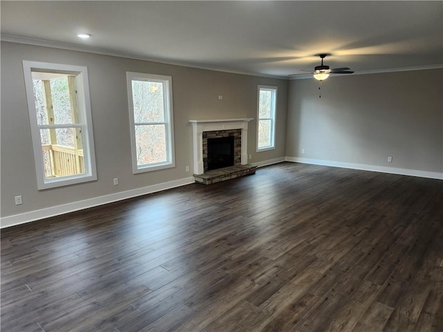 unfurnished living room with ornamental molding, dark wood finished floors, a stone fireplace, and baseboards