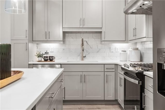 kitchen with gray cabinetry, under cabinet range hood, a sink, light countertops, and appliances with stainless steel finishes