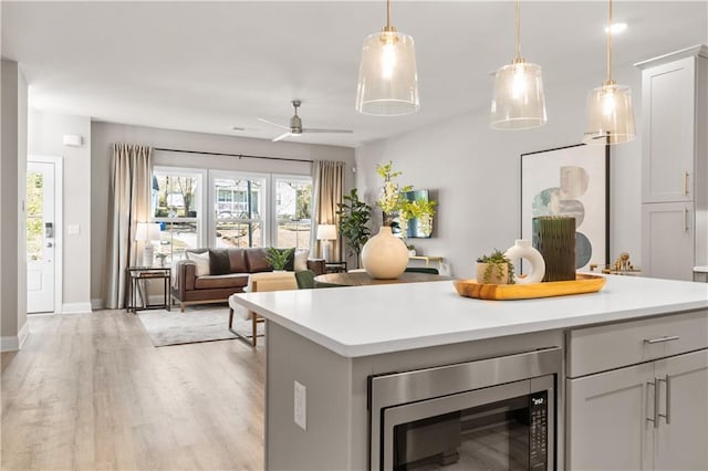 kitchen with ceiling fan, stainless steel microwave, open floor plan, light countertops, and light wood-style floors