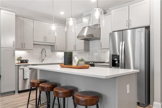 kitchen with wall chimney exhaust hood, appliances with stainless steel finishes, a center island, decorative light fixtures, and light countertops