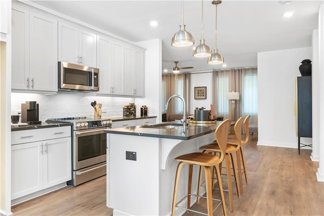 kitchen featuring decorative backsplash, a ceiling fan, dark countertops, a sink, and stainless steel appliances