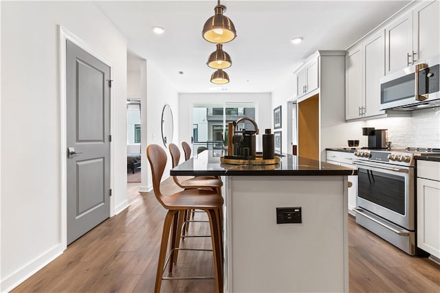 kitchen featuring appliances with stainless steel finishes, tasteful backsplash, a kitchen bar, and wood finished floors