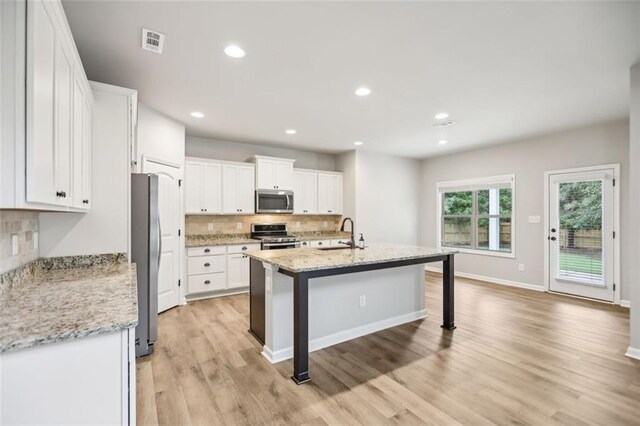 kitchen with sink, light hardwood / wood-style flooring, appliances with stainless steel finishes, light stone counters, and white cabinetry