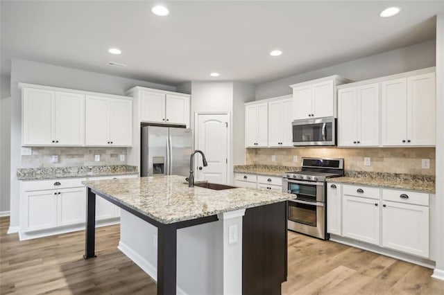 kitchen with backsplash, a kitchen island with sink, light hardwood / wood-style flooring, white cabinetry, and stainless steel appliances