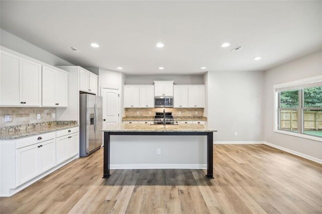 kitchen with light stone countertops, appliances with stainless steel finishes, decorative backsplash, white cabinets, and light wood-type flooring