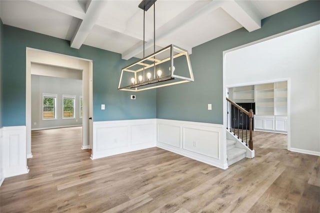 unfurnished dining area featuring beamed ceiling, an inviting chandelier, and light hardwood / wood-style flooring