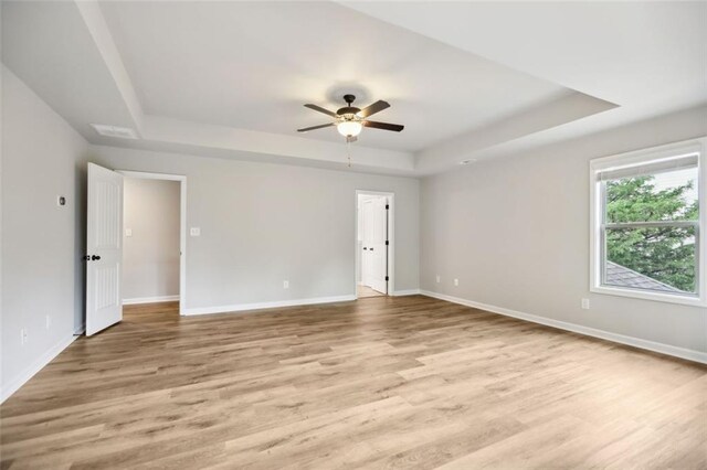 empty room featuring ceiling fan, light hardwood / wood-style floors, and a tray ceiling