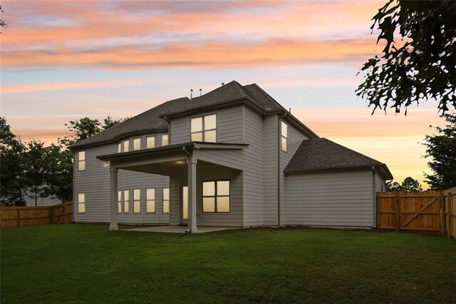 back house at dusk featuring a patio area and a yard