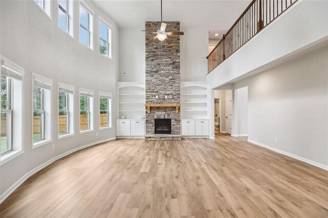 unfurnished living room with ceiling fan, a towering ceiling, a fireplace, built in features, and light hardwood / wood-style floors