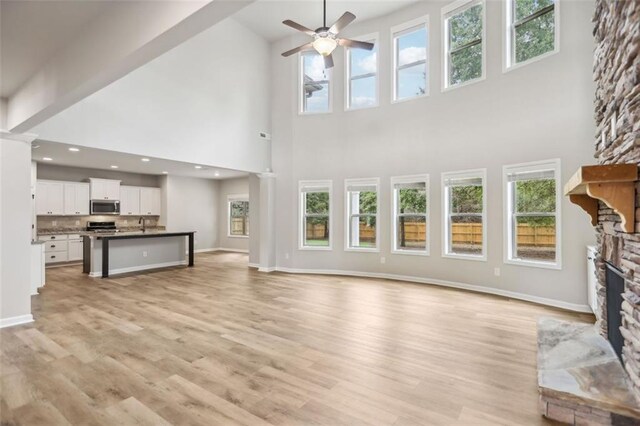 unfurnished living room featuring a stone fireplace, ceiling fan, light hardwood / wood-style flooring, and high vaulted ceiling