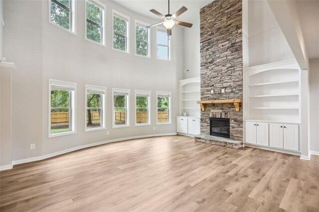 unfurnished living room with a fireplace, light wood-type flooring, a towering ceiling, and built in features