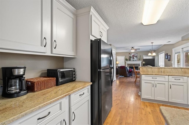 kitchen featuring white cabinets, black refrigerator, ceiling fan, decorative light fixtures, and light hardwood / wood-style floors