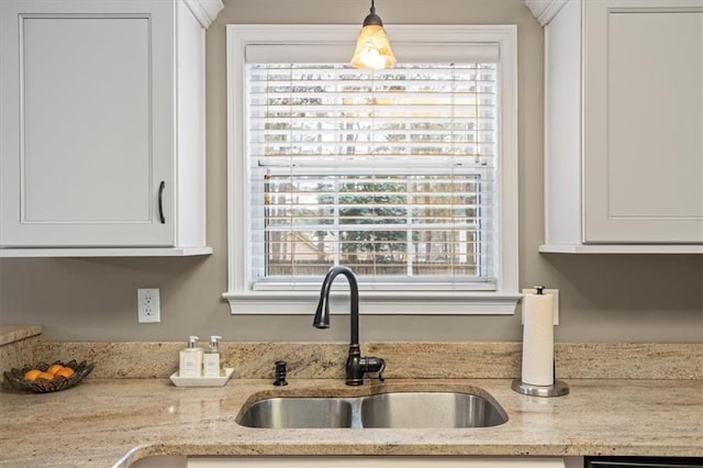 kitchen featuring light stone countertops, white cabinetry, sink, and hanging light fixtures