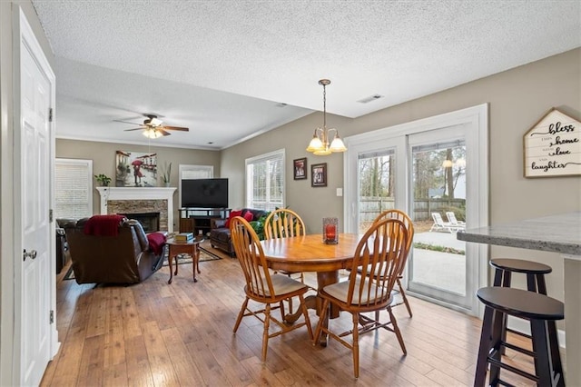 dining area with a textured ceiling, ceiling fan with notable chandelier, light wood-type flooring, and a fireplace