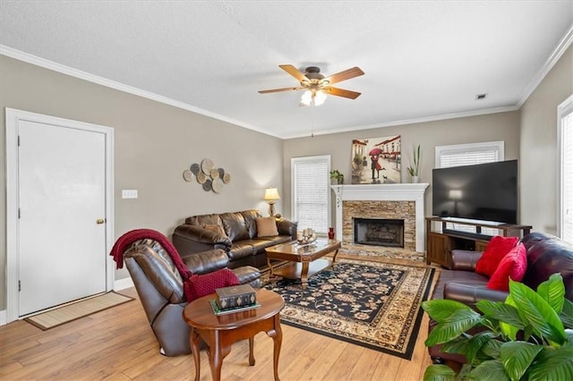 living room featuring crown molding, a fireplace, ceiling fan, and light hardwood / wood-style floors