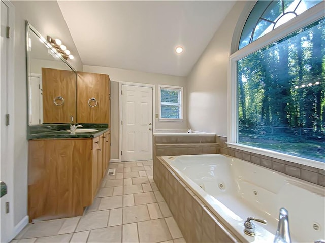 bathroom featuring plenty of natural light, vaulted ceiling, tiled tub, and vanity