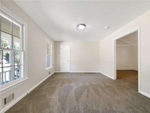 spare room with plenty of natural light and dark colored carpet