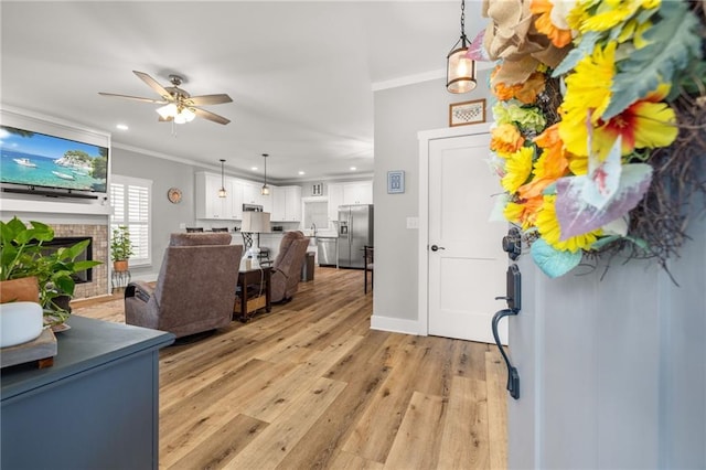 foyer entrance with a tiled fireplace, ornamental molding, ceiling fan, and light wood-type flooring