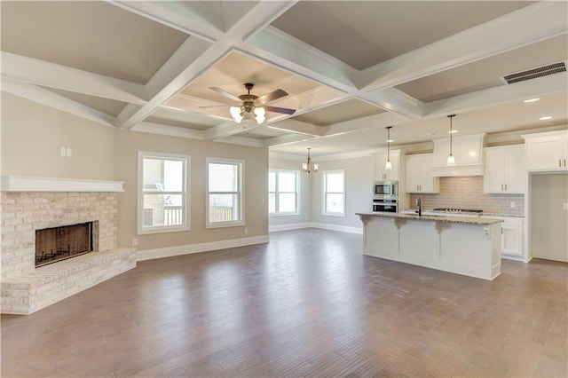 kitchen with an island with sink, ceiling fan, coffered ceiling, wood-type flooring, and beam ceiling