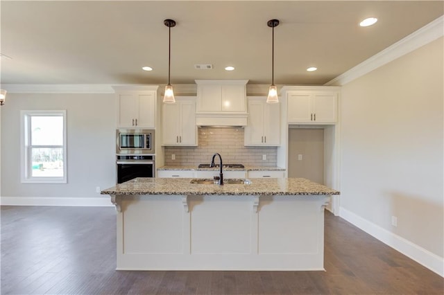 kitchen featuring appliances with stainless steel finishes, dark wood-type flooring, light stone counters, crown molding, and a kitchen island with sink