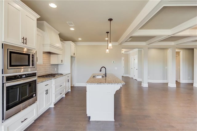 kitchen featuring pendant lighting, appliances with stainless steel finishes, backsplash, a center island with sink, and dark wood-type flooring