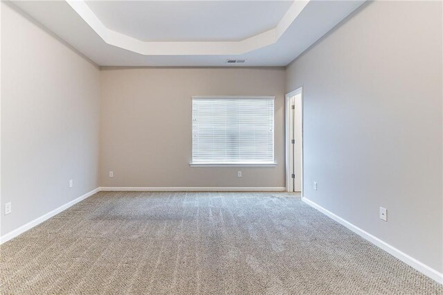 unfurnished room with a tray ceiling, carpet flooring, visible vents, and baseboards